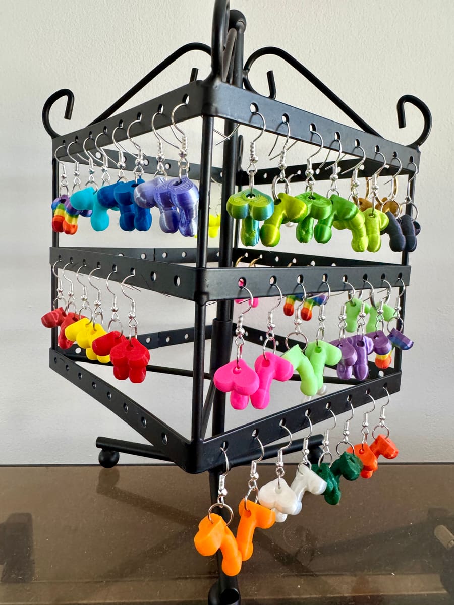 Colorful GeoGenitals charm earrings on a display stand